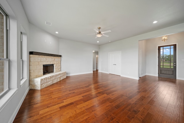 unfurnished living room featuring a stone fireplace, dark wood-type flooring, and ceiling fan with notable chandelier