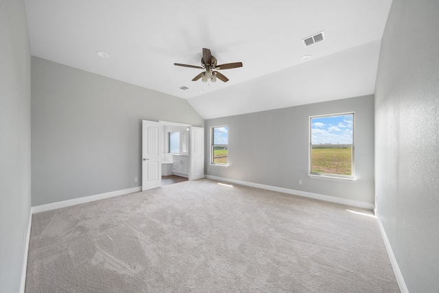 unfurnished bedroom featuring vaulted ceiling, multiple windows, light colored carpet, and ceiling fan