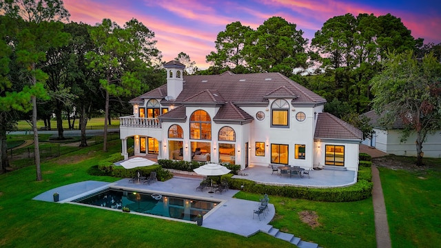 back house at dusk featuring a patio and a lawn