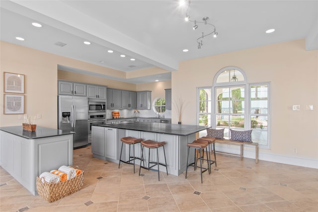 kitchen with light tile patterned floors, appliances with stainless steel finishes, gray cabinets, and a kitchen island