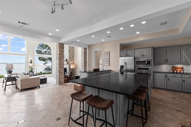 kitchen with decorative backsplash, gray cabinets, appliances with stainless steel finishes, light tile patterned floors, and a center island