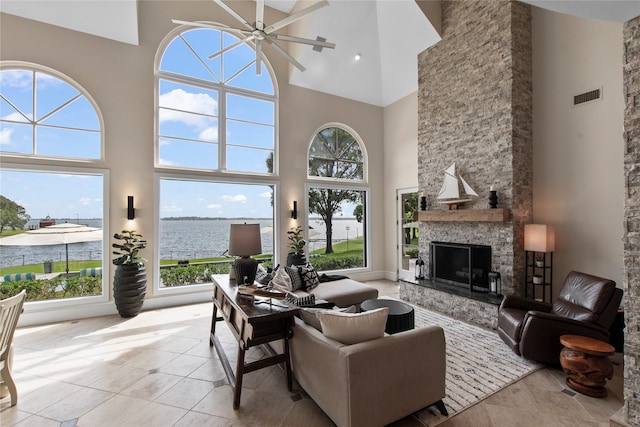 tiled living room with ceiling fan, a fireplace, a high ceiling, and a water view