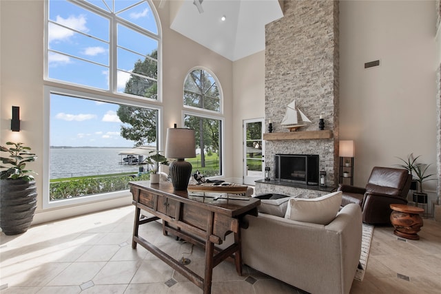 tiled living room featuring a stone fireplace, a high ceiling, and a water view