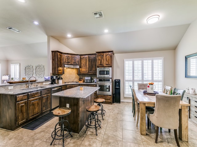 kitchen with stainless steel appliances, sink, light stone countertops, vaulted ceiling, and a kitchen island