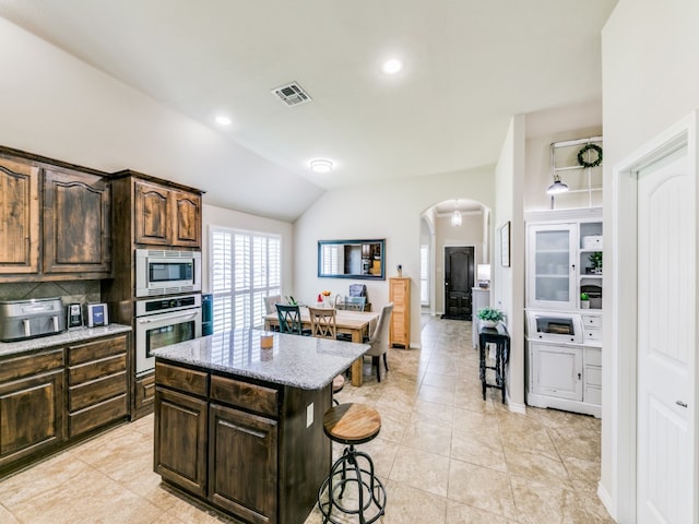 kitchen featuring light tile patterned flooring, decorative backsplash, a center island, vaulted ceiling, and appliances with stainless steel finishes