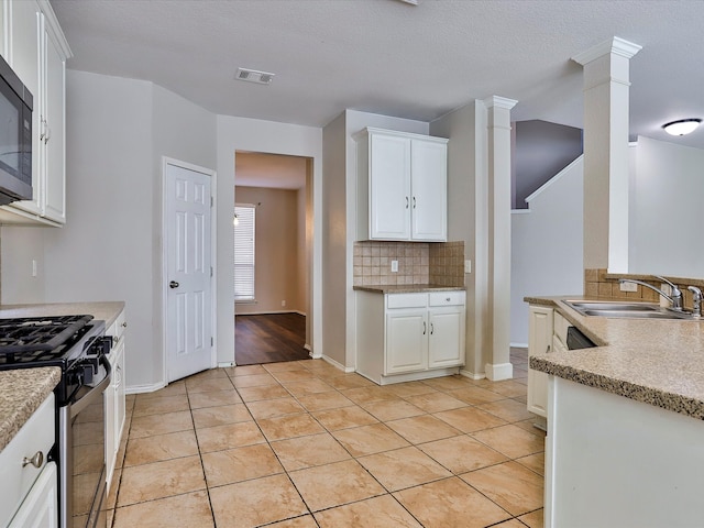 kitchen featuring white cabinets, sink, appliances with stainless steel finishes, decorative columns, and light tile patterned floors