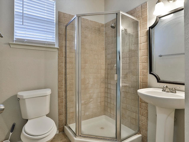 bathroom featuring a shower with door, sink, and toilet