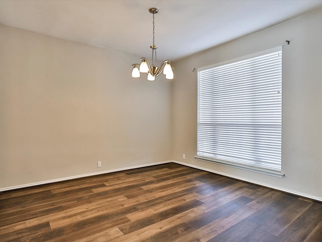 spare room featuring an inviting chandelier and dark hardwood / wood-style floors