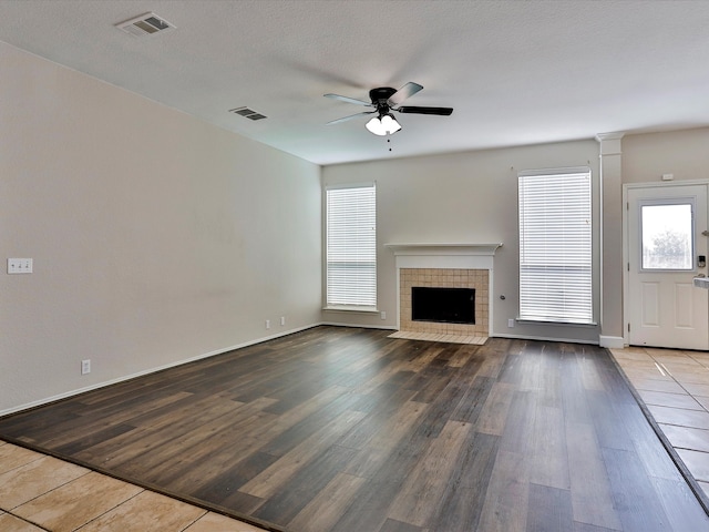 unfurnished living room featuring ceiling fan, hardwood / wood-style flooring, a tiled fireplace, and a textured ceiling