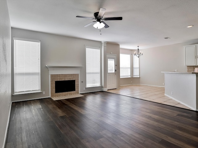 unfurnished living room featuring ceiling fan with notable chandelier, hardwood / wood-style flooring, and a fireplace