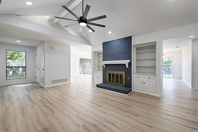 unfurnished living room with a wealth of natural light, lofted ceiling with beams, a brick fireplace, and light wood-type flooring