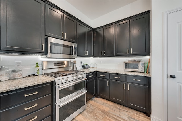 kitchen featuring appliances with stainless steel finishes, tasteful backsplash, light wood-type flooring, and light stone countertops