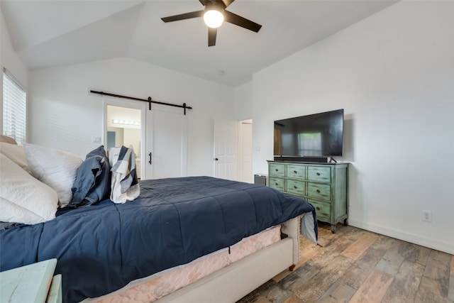 bedroom with lofted ceiling, a barn door, ceiling fan, ensuite bathroom, and hardwood / wood-style flooring