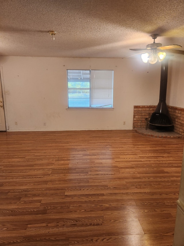 unfurnished living room featuring ceiling fan, a textured ceiling, dark hardwood / wood-style floors, and a wood stove