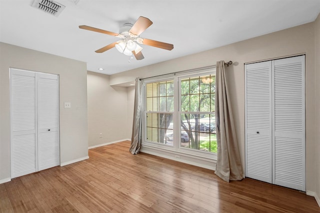 unfurnished bedroom featuring light hardwood / wood-style flooring, multiple closets, and ceiling fan