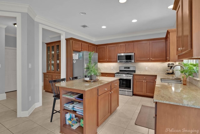 kitchen with light stone countertops, sink, appliances with stainless steel finishes, a kitchen island, and ornamental molding