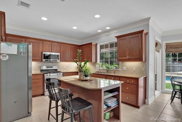 kitchen with sink, stainless steel appliances, light tile patterned floors, crown molding, and a kitchen island