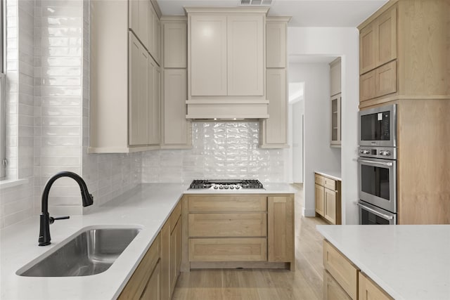 kitchen featuring stainless steel gas stovetop, backsplash, light hardwood / wood-style flooring, sink, and light brown cabinets