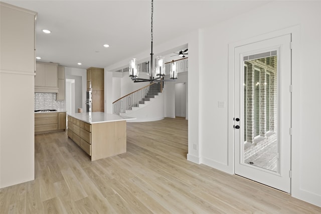 kitchen featuring ceiling fan with notable chandelier, tasteful backsplash, hanging light fixtures, gas cooktop, and light wood-type flooring