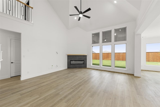 unfurnished living room with a wealth of natural light, high vaulted ceiling, ceiling fan, and a tile fireplace