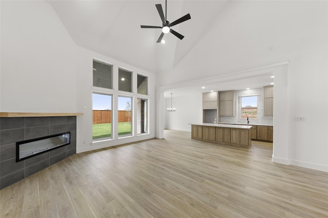 unfurnished living room featuring light hardwood / wood-style floors, high vaulted ceiling, ceiling fan, and a tile fireplace