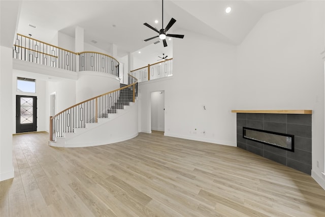 unfurnished living room featuring a tiled fireplace, high vaulted ceiling, ceiling fan, and light hardwood / wood-style floors