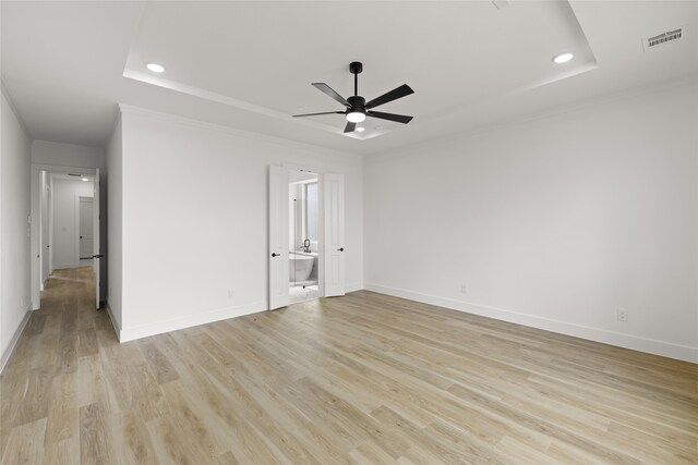 unfurnished bedroom with a tray ceiling, ceiling fan, ensuite bath, and light hardwood / wood-style flooring