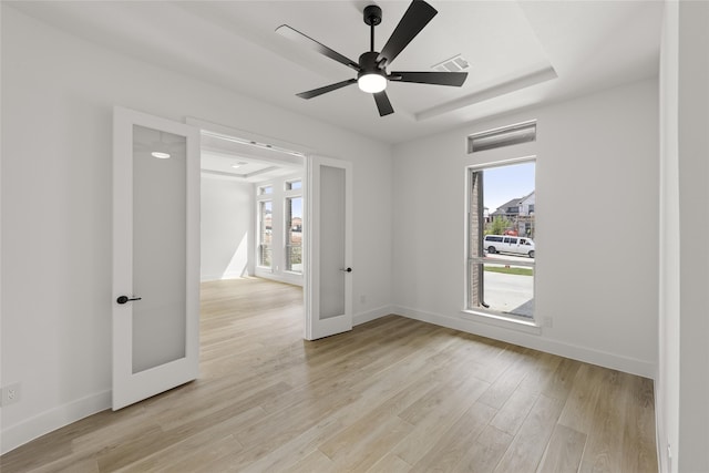 spare room featuring french doors, light hardwood / wood-style flooring, a raised ceiling, and ceiling fan