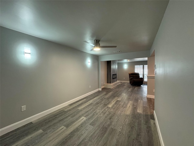unfurnished living room featuring a glass covered fireplace, baseboards, a ceiling fan, and dark wood-type flooring