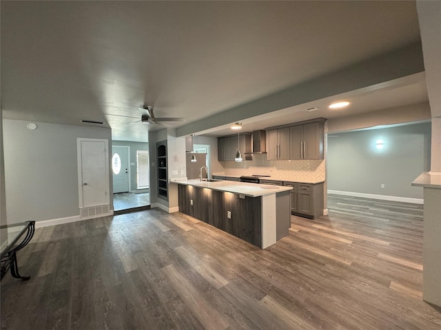 kitchen with wall chimney range hood, light countertops, a ceiling fan, baseboards, and dark wood-style floors