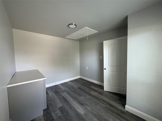 unfurnished room featuring baseboards, attic access, and dark wood-type flooring