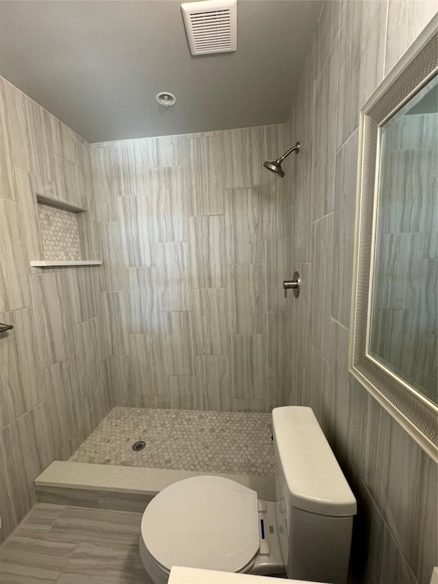 full bath with toilet, visible vents, and tiled shower