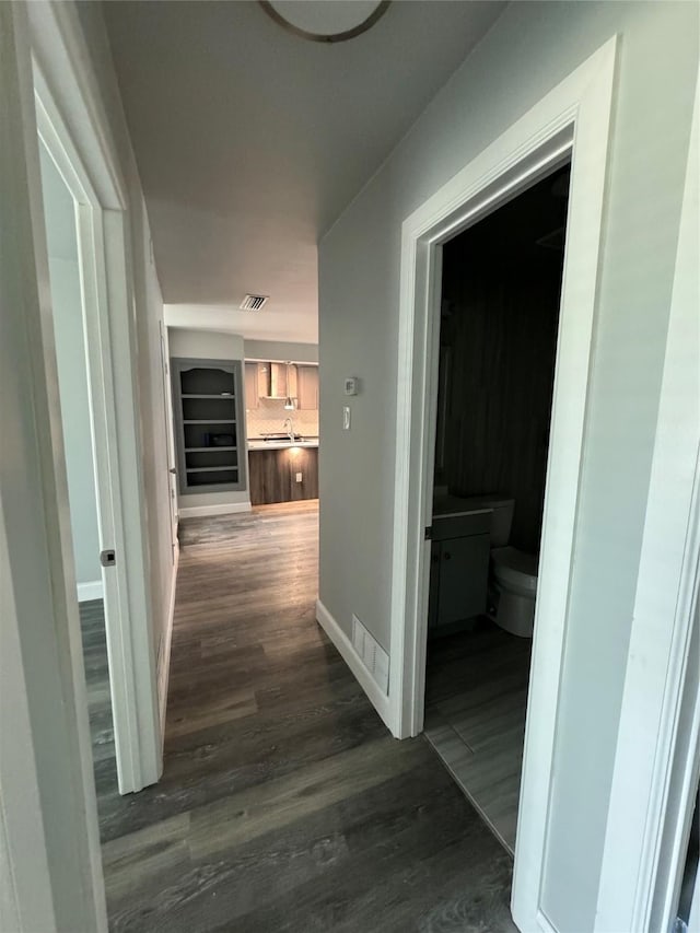 hallway with baseboards, visible vents, and dark wood-type flooring