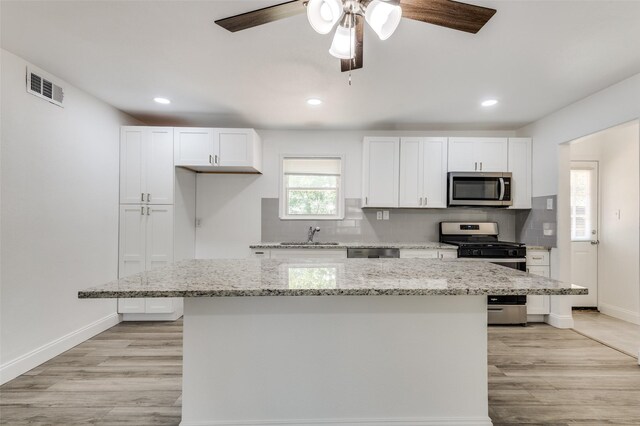 kitchen with stainless steel appliances, white cabinetry, ceiling fan, and a center island