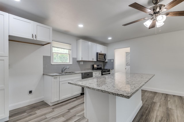 kitchen with light stone countertops, appliances with stainless steel finishes, white cabinets, and a sink