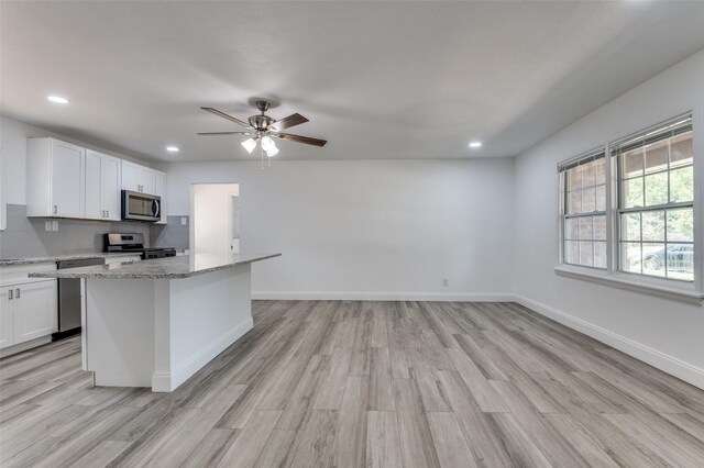 kitchen with light stone counters, light hardwood / wood-style floors, white cabinets, stainless steel appliances, and ceiling fan