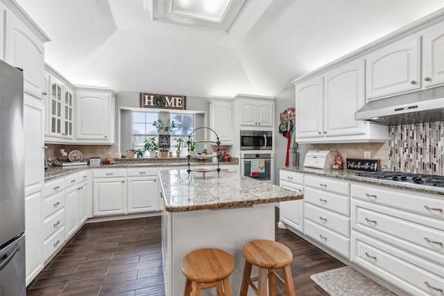 kitchen featuring a kitchen bar, stainless steel appliances, light stone counters, backsplash, and a kitchen island