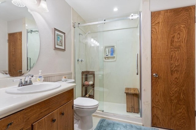 full bathroom with a stall shower, a wainscoted wall, vanity, and toilet