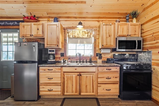 kitchen featuring appliances with stainless steel finishes, light brown cabinets, a sink, and wooden walls