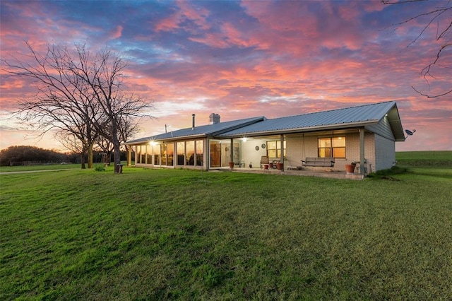 back of property with a lawn, a patio, a chimney, metal roof, and brick siding