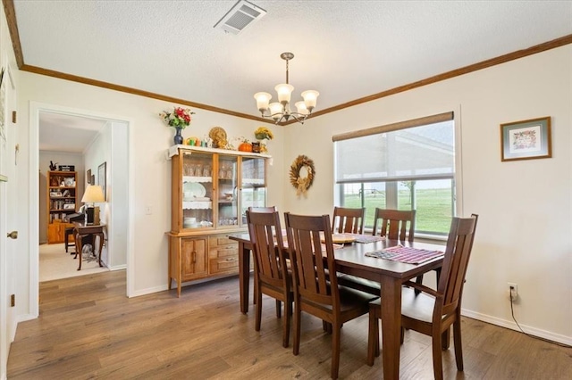 dining area with visible vents, a textured ceiling, crown molding, light wood-style floors, and a chandelier