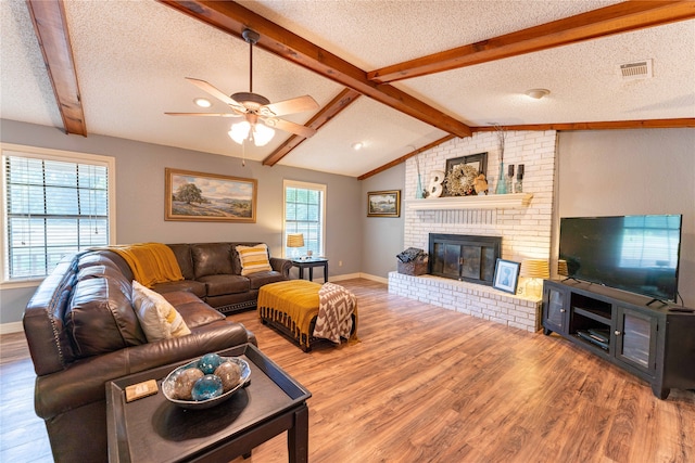 living room with ceiling fan, wood-type flooring, a brick fireplace, and a textured ceiling