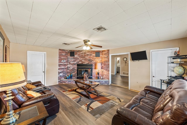 living room featuring dark hardwood / wood-style floors, a brick fireplace, brick wall, and ceiling fan