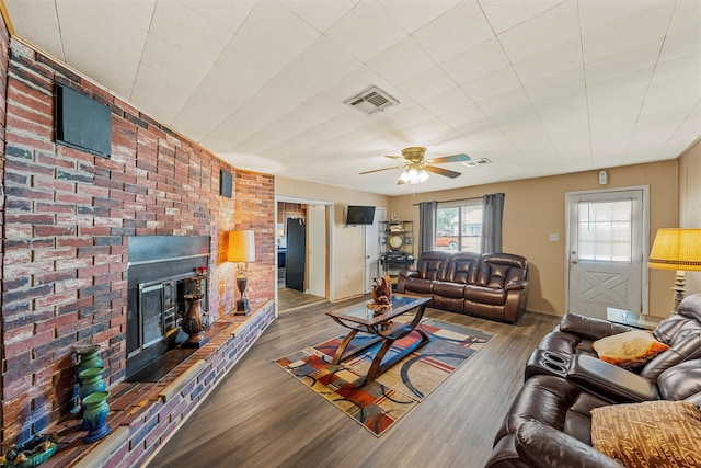 living room featuring wood-type flooring, a brick fireplace, brick wall, and ceiling fan