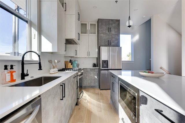 kitchen featuring pendant lighting, sink, white cabinetry, appliances with stainless steel finishes, and light wood-type flooring