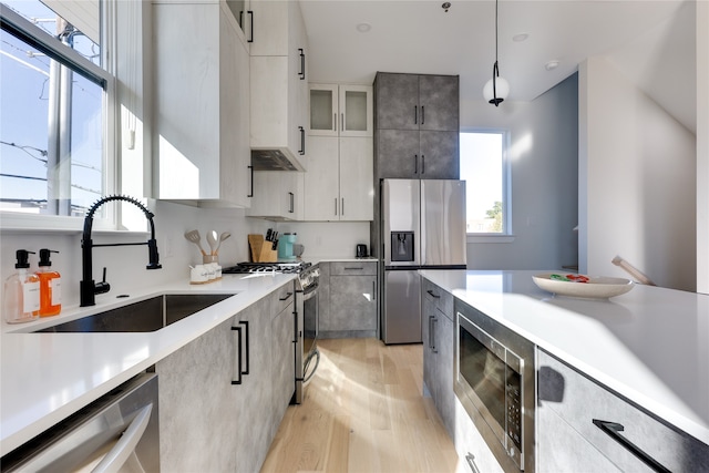 kitchen with hanging light fixtures, white cabinets, stainless steel appliances, light hardwood / wood-style flooring, and sink