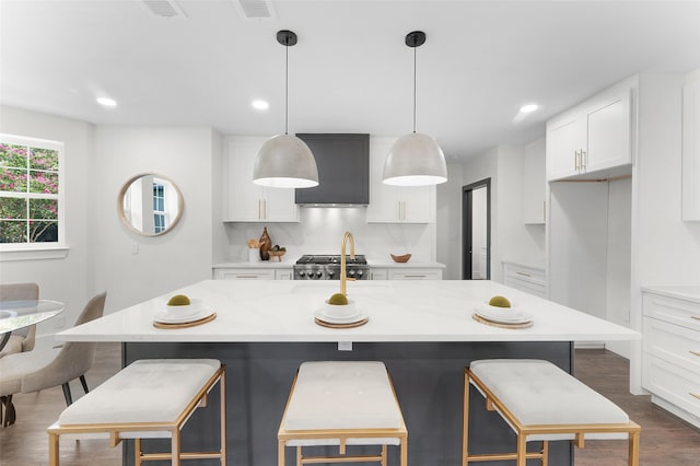 kitchen with an island with sink, decorative backsplash, white cabinets, dark hardwood / wood-style flooring, and pendant lighting