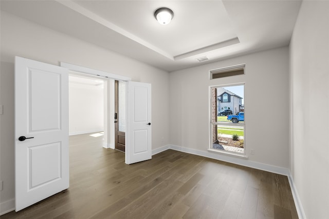 unfurnished room with a raised ceiling and dark wood-type flooring