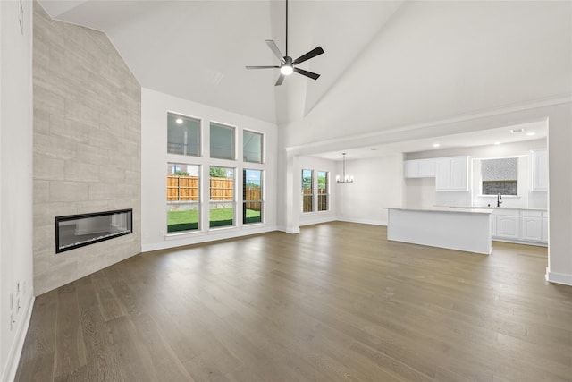 unfurnished living room with ceiling fan with notable chandelier, sink, a tile fireplace, hardwood / wood-style flooring, and high vaulted ceiling