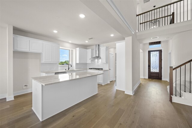 kitchen with white cabinetry, a center island, wall chimney exhaust hood, light stone countertops, and dark hardwood / wood-style flooring